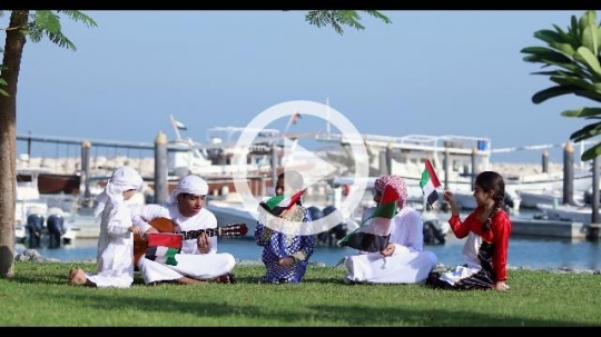 Arab siblings sitting on the grass celebrating the UAE National Day together|