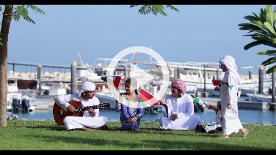 Middle Eastern siblings sitting together on the grass celebrating the UAE National Day|