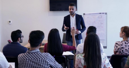 Woman raises her hand in class to ask a question |-