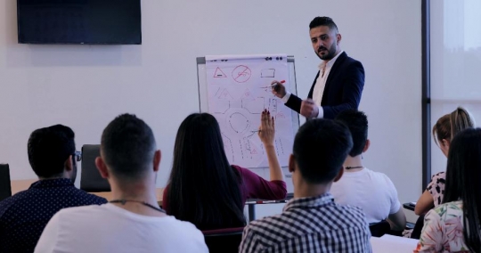 Woman raises her hand in the classroom to ask the professor a question |-