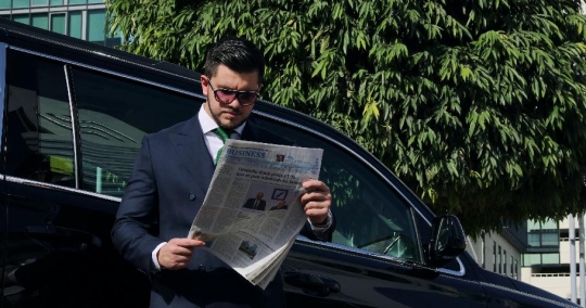 Businessman leaning on the car reading the newspaper|-