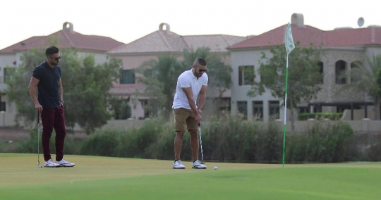 Middle Eastern man watching his friend play golf|-
