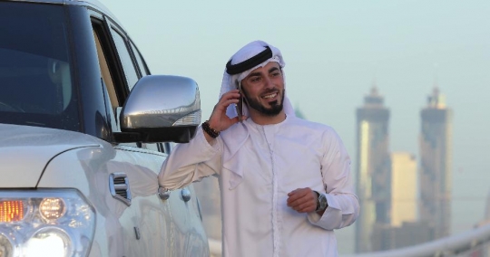 Middle Eastern man standing next to his car talking on the phone|-