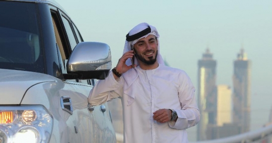 Middle Eastern man standing by his car talking on the phone|-