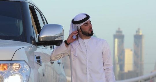 Middle eastern man leaning on his car talking on the phone|-
