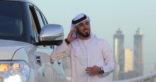 Arab man steps out of his car and talks on the phone|-