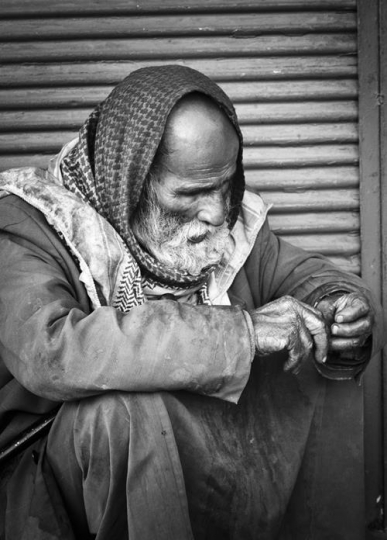 black and white image of poor senior man sitting in a street