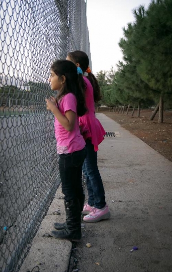 two girls looking through a chain-link fence