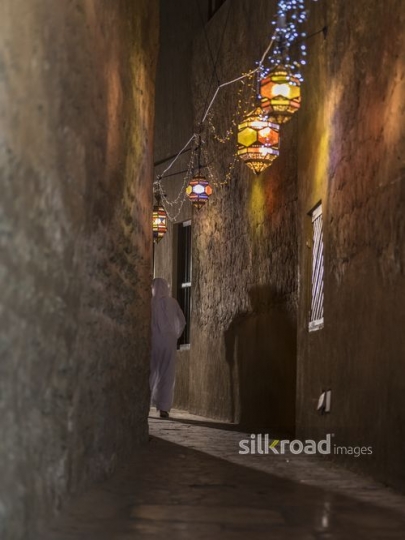 Arab man walking through the pathway decorated with Ramadan lanterns|-