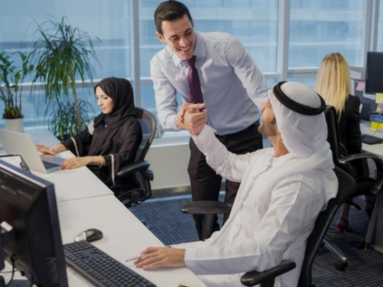 Business men smiling and shaking hands with other employees behind them|