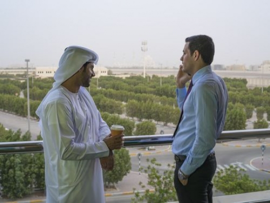 A businessman is having a phone call outside while his employee is having coffee at the balcony