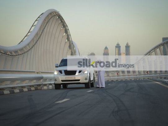 Middle Eastern man parked on the side of the road calling for help|