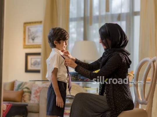 Middle Eastern woman fixing her the young boys tie before school|