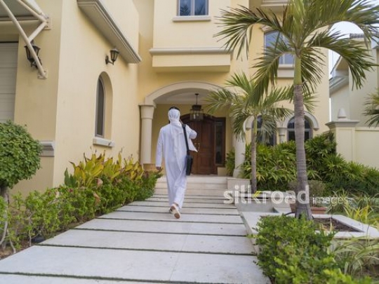 Arab man walking towards the house on the phone|