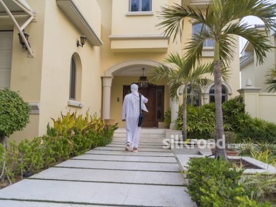 Middle Eastern man walking towards the house on the phone|