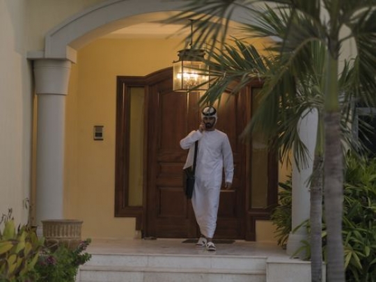 Arabian man talking on the phone while leaving his house|-