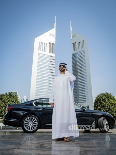 Middle Eastern man standing wearing his sunglasses using his mobile|-