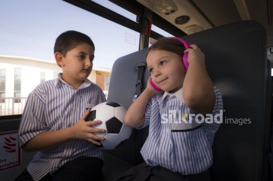 Arab Student carrying a football looking at the Western Student listening to music|-