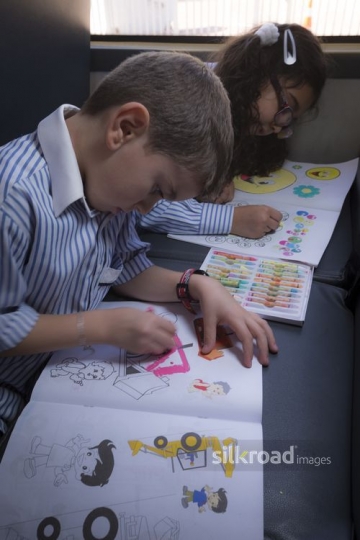 Kids sitting down on the bus coloring |-
