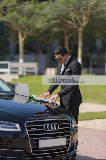 Businessman standing by his car doing work from his laptop|