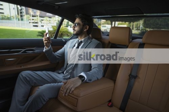Businessman sitting inside a luxury car using his mobile|