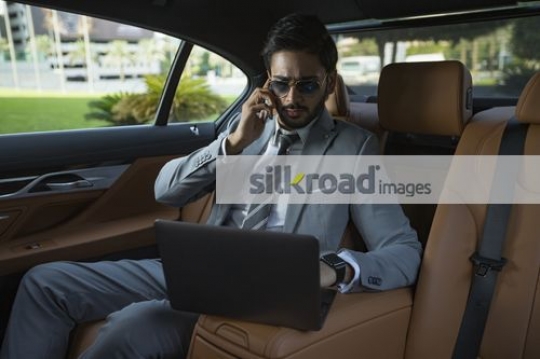 Businessman sitting in the backseat of the car doing work|