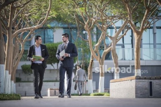 Middle Eastern Businessman and Western Businessman both carrying folders walking together|-