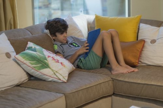 Arabian boy sitting down on the couch playing on his device|-