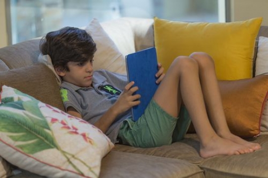 Arab boy sitting on the couch playing on his device|-