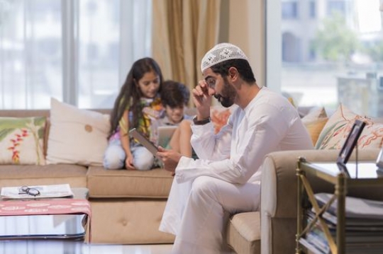 Arab father and kids sitting on their devices in the living room|-