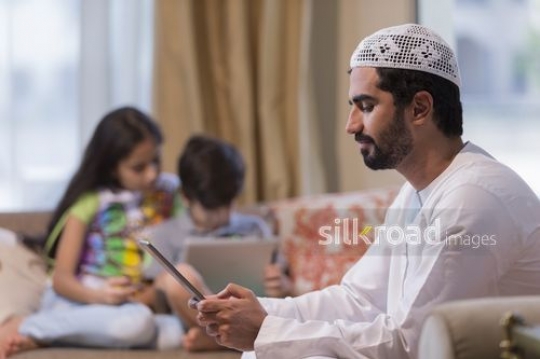 Middle Eastern man on the device and the kids using their devices in the background|