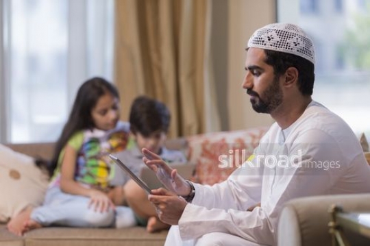 Middle Eastern man on the device with the kids are in the background |