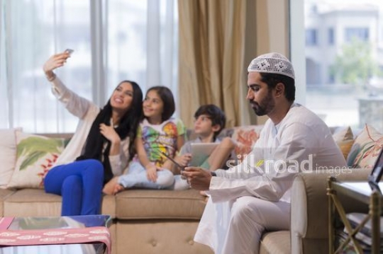 Middle Eastern woman taking a selfie with the kids and the man on the device|
