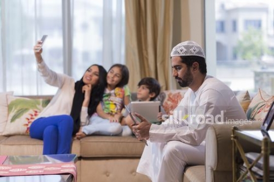Middle Eastern woman taking a selfie with the young kids and the man on the device|
