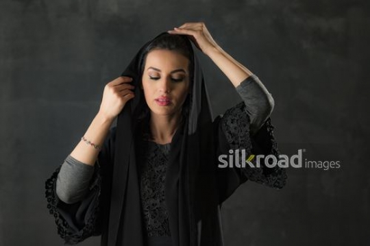 Arab woman dressed in the traditional attire fixing her shayla|