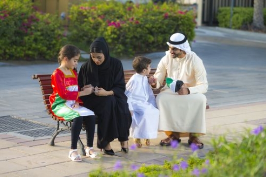 Mother helping her kid with the bracelets while the father is talking to the little boy|-