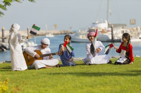Arab boy standing while the rest are singing along to the teenager playing the guitar|-