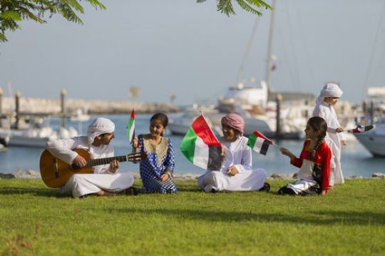 Arab boy walking around the teenagers and kids while singing along for national day|-