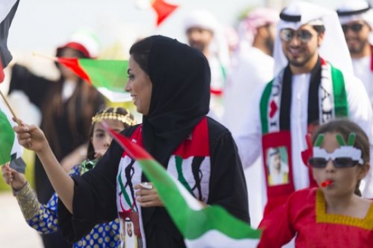 Arab woman carrying a UAE flag during a National day parade|
