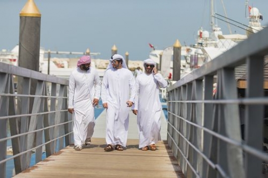 Arab man talking on the phone while walking with his friends on the dock|