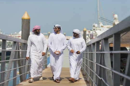 Arab men dressed in the traditional UAE attire walking on the dock|