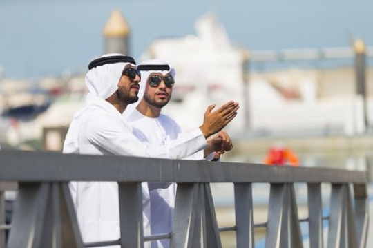 Arab men dressed in the traditional UAE attire standing by the dock|