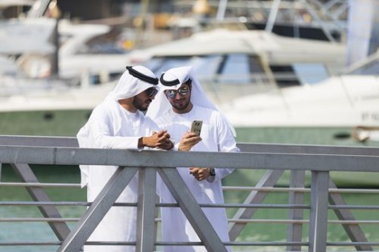 Men dressed in the traditional UAE attire standing by the dock talking to each other|
