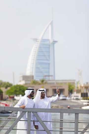 Men dressed in the traditional UAE attire standing by the dock taking a picture together|
