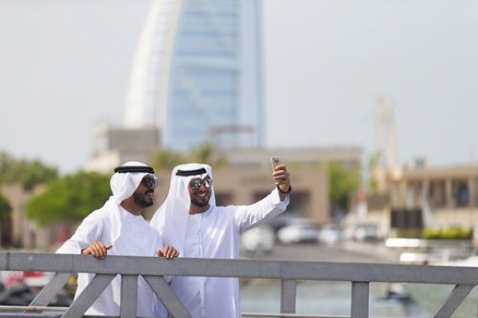 Arab men standing by the dock with a background of burj al arab taking a picture together|