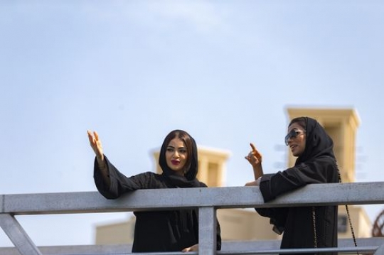 Arab friends dressed in the traditional woman UAE attire standing by the dock talking to each other|