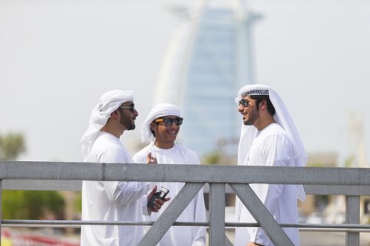 Three men dressed in the traditional UAE attire standing by the dock talking to each other|