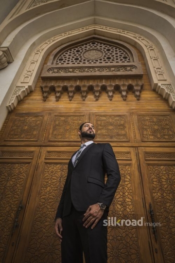 Middle Eastern Businessman standing infront of a brown gate|-