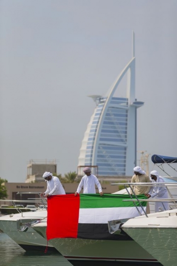 Middle eastern men dressed in the traditional attire holding a UAE flag on the yacht to celebrate National Day|