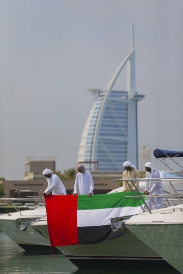 Arab men standing by the yacht holding a UAE flag with a background of a well-known landmark|